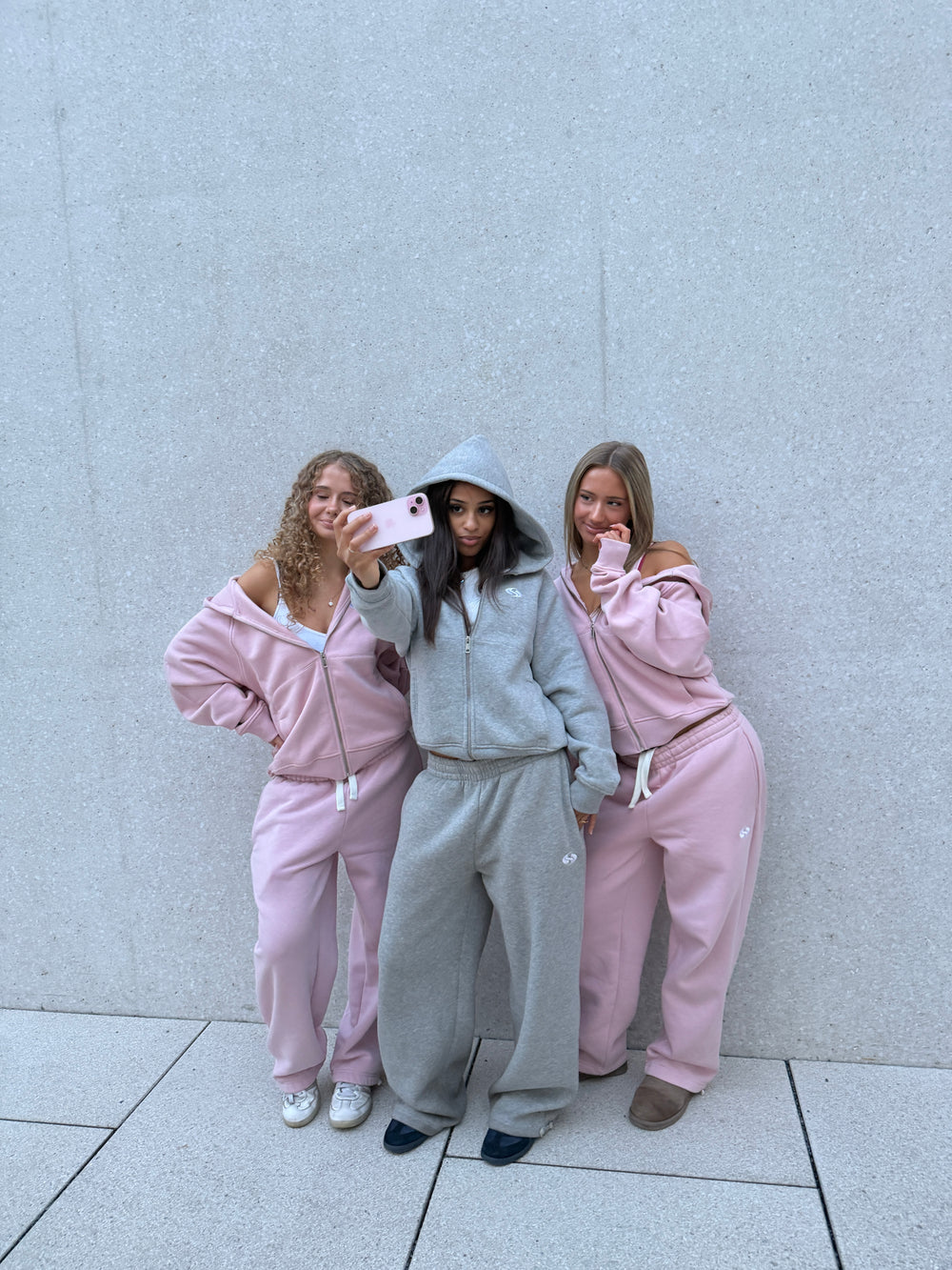 Drei Freundinnen in Sportz Sets in Rosé und Grau machen ein Selfie