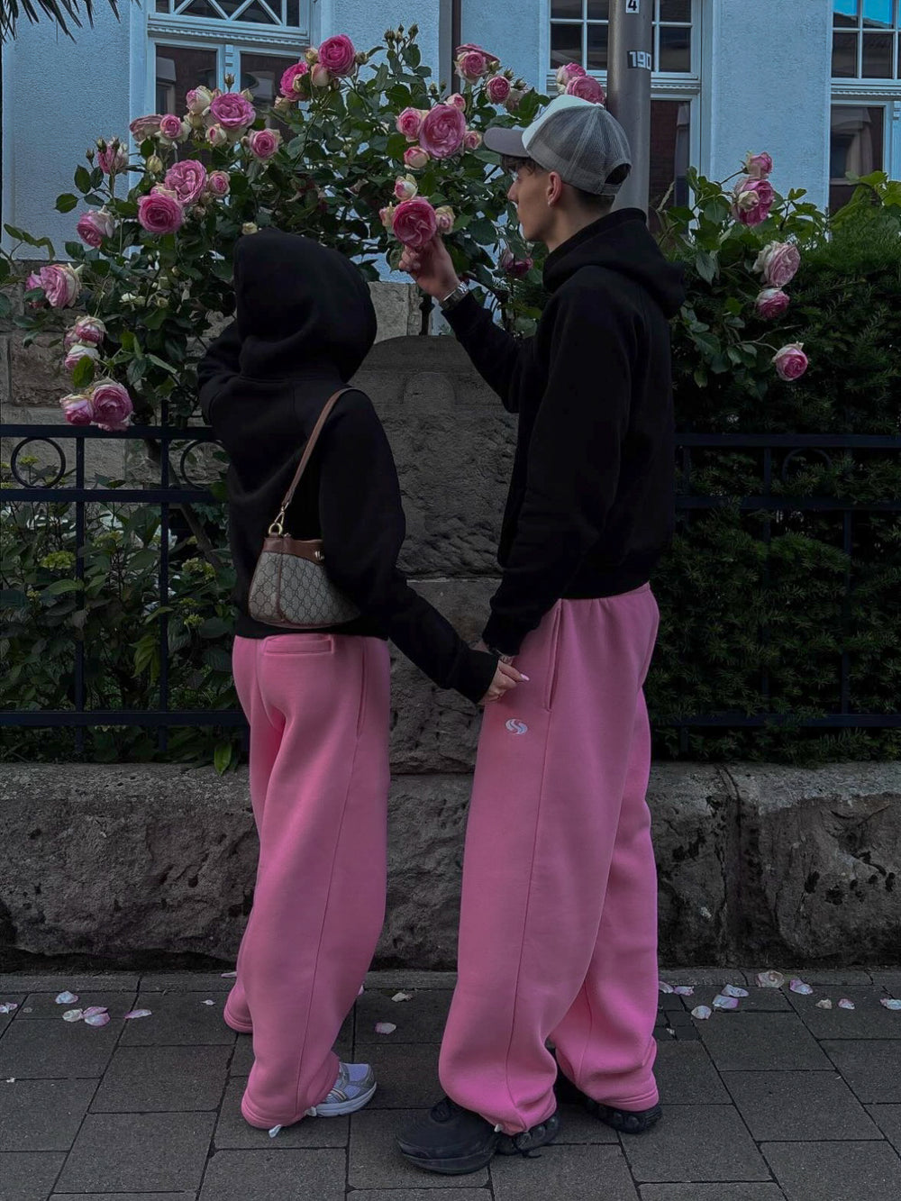 Paar in schwarzen Hoodies und pinken Sportz Joggern vor Rosen